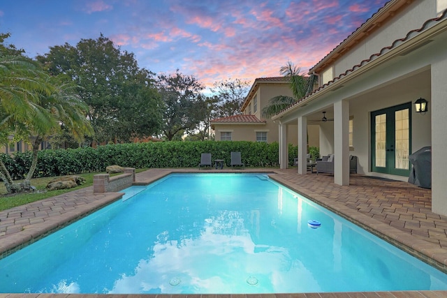 pool at dusk with ceiling fan, a patio area, grilling area, and french doors