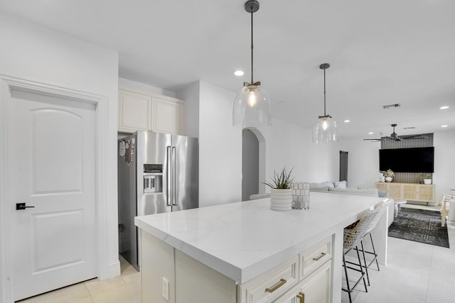 kitchen featuring light stone countertops, stainless steel refrigerator with ice dispenser, light tile patterned floors, a center island, and hanging light fixtures