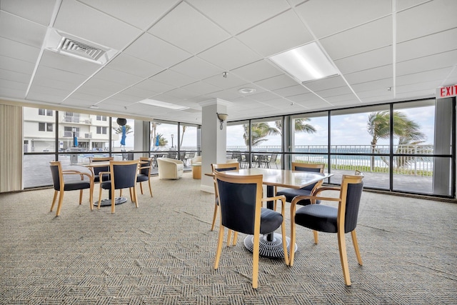 carpeted dining room with a paneled ceiling, plenty of natural light, a water view, and a wall of windows