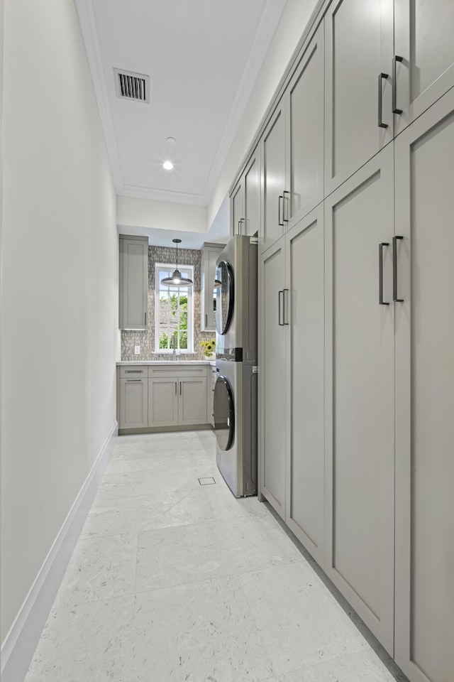 laundry area with cabinets, ornamental molding, stacked washer and clothes dryer, and sink