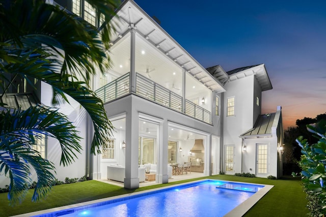 back house at dusk featuring outdoor lounge area, a yard, a balcony, and a patio