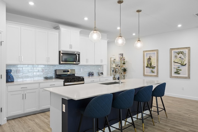 kitchen featuring decorative light fixtures, sink, white cabinets, stainless steel appliances, and a center island with sink