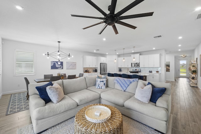 living room with sink, ceiling fan with notable chandelier, and light wood-type flooring