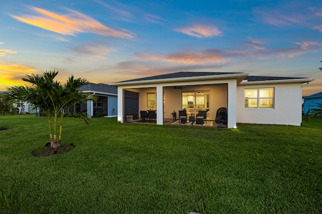 back house at dusk featuring a patio area, ceiling fan, and a lawn