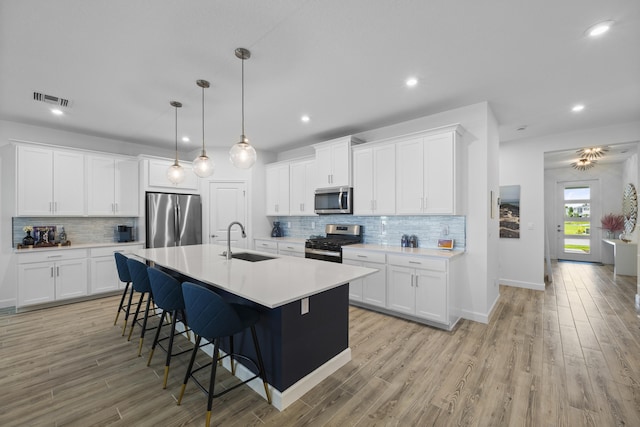 kitchen with sink, white cabinetry, hanging light fixtures, stainless steel appliances, and an island with sink