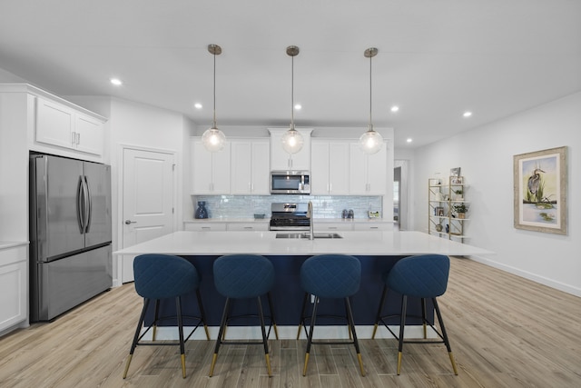 kitchen featuring an island with sink, white cabinetry, sink, hanging light fixtures, and stainless steel appliances