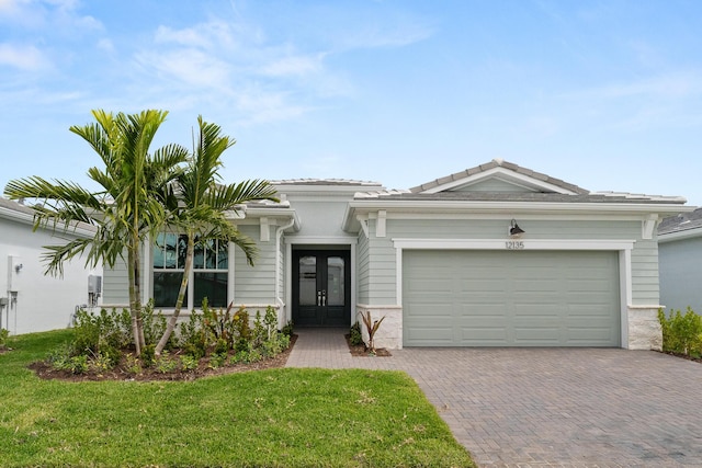 view of front of property featuring french doors, decorative driveway, a garage, and a front lawn