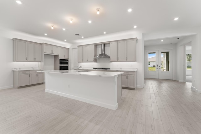 kitchen with light wood-style flooring, gray cabinets, a sink, stovetop, and wall chimney exhaust hood