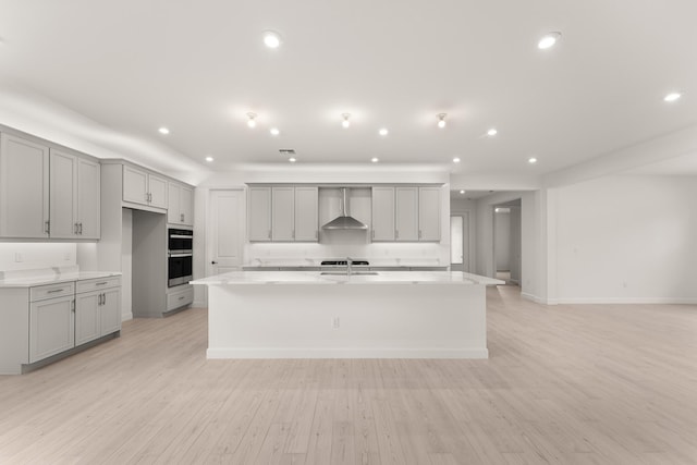 kitchen featuring wall chimney range hood, gray cabinets, light wood finished floors, and a spacious island