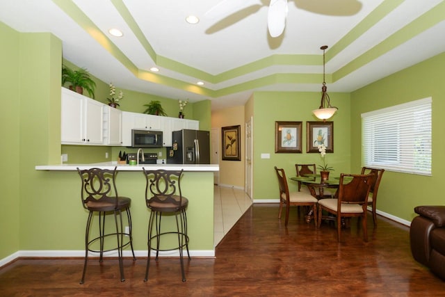 kitchen with white cabinetry, dark hardwood / wood-style flooring, kitchen peninsula, a kitchen bar, and appliances with stainless steel finishes