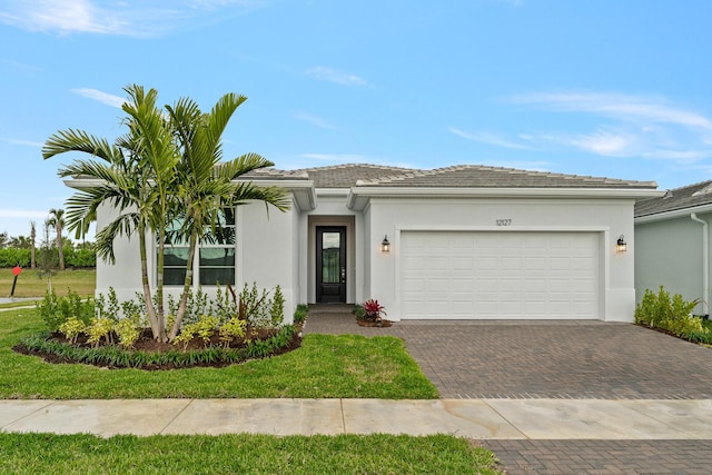 view of front of property with a tiled roof, decorative driveway, a garage, and stucco siding