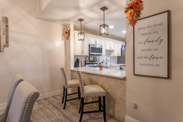 kitchen with hanging light fixtures, light hardwood / wood-style floors, a breakfast bar area, white cabinets, and appliances with stainless steel finishes