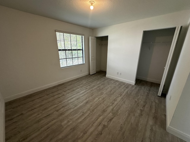 unfurnished bedroom featuring dark hardwood / wood-style flooring, a textured ceiling, and multiple closets