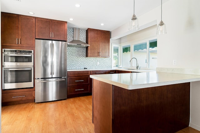 kitchen featuring sink, appliances with stainless steel finishes, hanging light fixtures, kitchen peninsula, and wall chimney exhaust hood