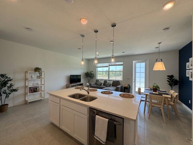 kitchen with pendant lighting, a kitchen island with sink, white cabinets, sink, and stainless steel dishwasher