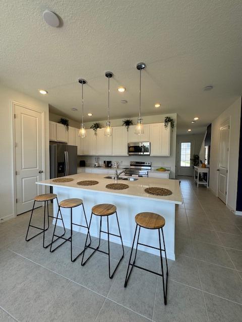 kitchen with white cabinetry, stainless steel appliances, a kitchen breakfast bar, an island with sink, and pendant lighting