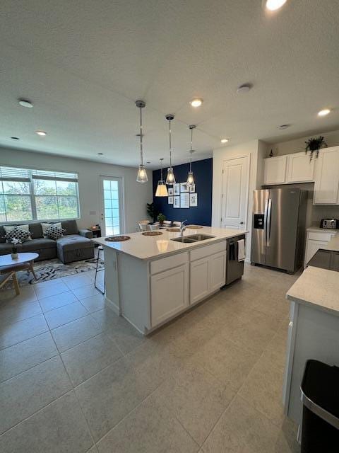 kitchen with appliances with stainless steel finishes, sink, pendant lighting, white cabinetry, and an island with sink