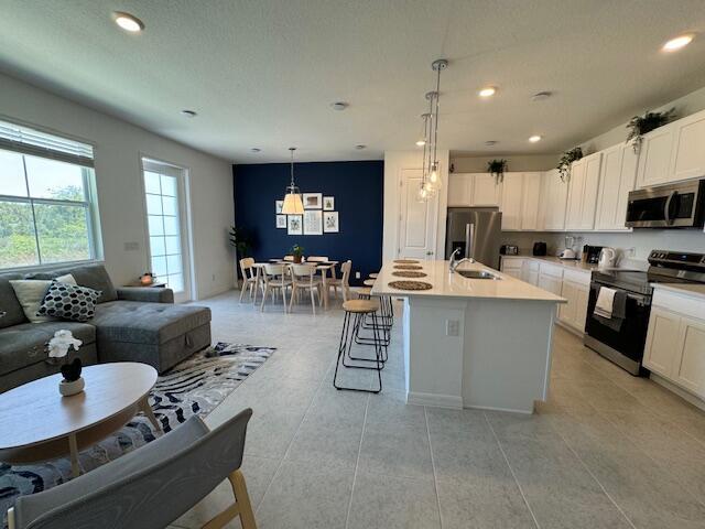 kitchen featuring a breakfast bar, stainless steel appliances, white cabinetry, hanging light fixtures, and an island with sink