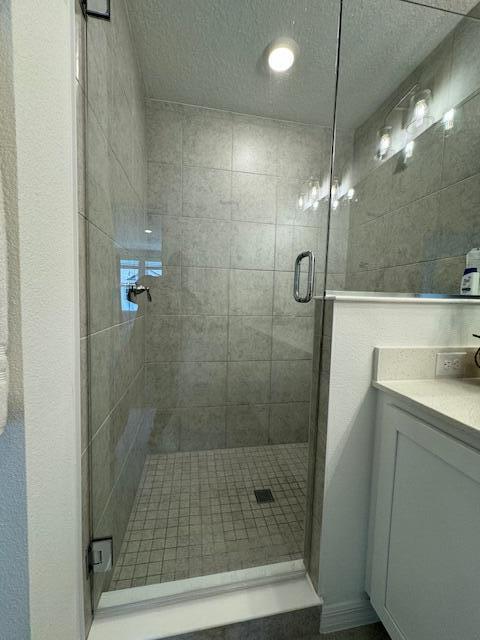 bathroom with vanity, a shower with shower door, and a textured ceiling