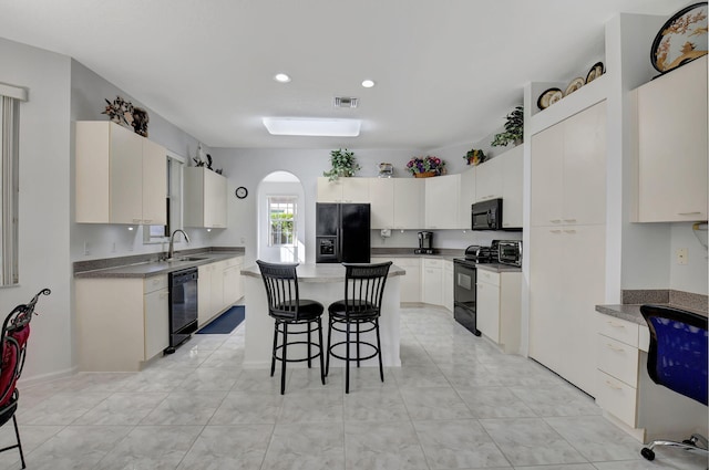 kitchen featuring black appliances, sink, a kitchen island, white cabinetry, and a breakfast bar area