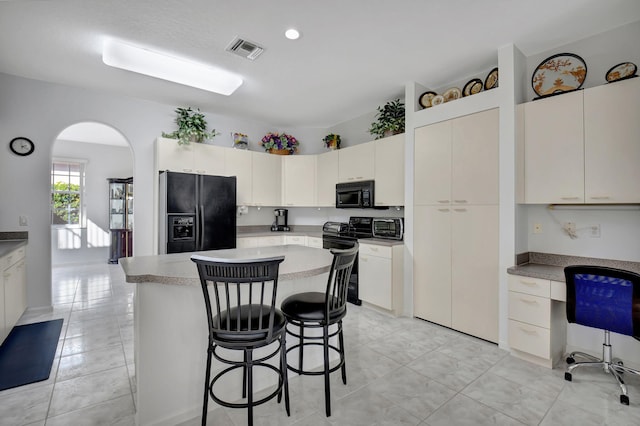 kitchen with a breakfast bar, a center island, black appliances, white cabinets, and light tile patterned floors