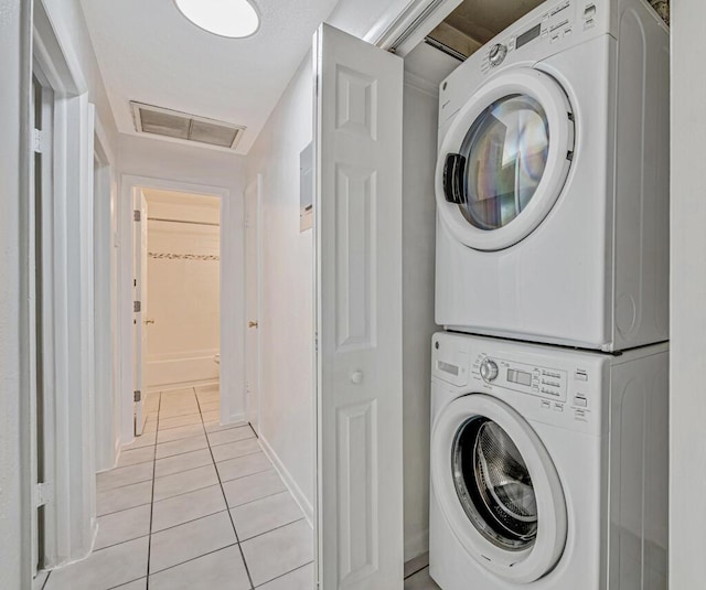 washroom with stacked washer / drying machine and light tile patterned flooring