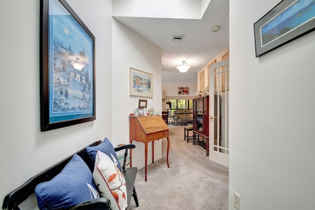 hallway with light carpet, visible vents, and a textured ceiling