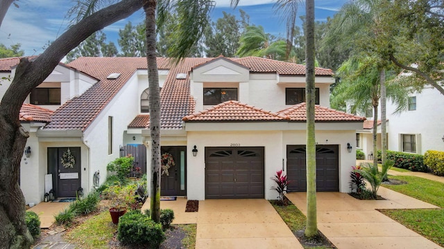 mediterranean / spanish home with a garage, a tile roof, concrete driveway, and stucco siding