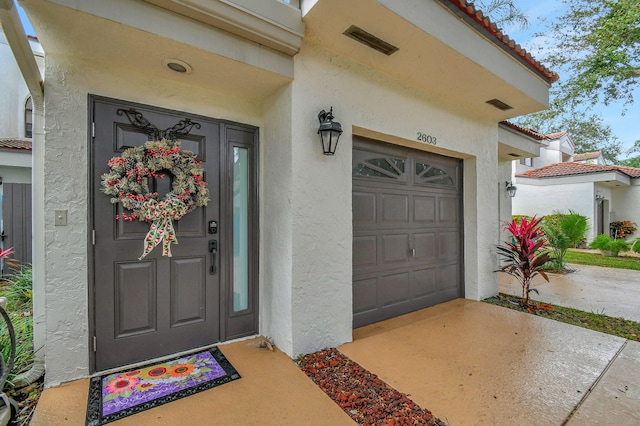 doorway to property featuring a garage, driveway, a tiled roof, and stucco siding