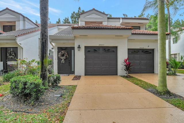 view of front of property with an attached garage, a tiled roof, concrete driveway, and stucco siding