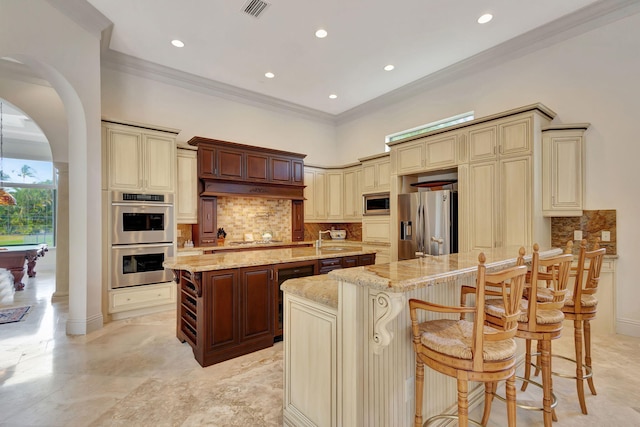 kitchen featuring a kitchen bar, appliances with stainless steel finishes, cream cabinetry, and a kitchen island with sink