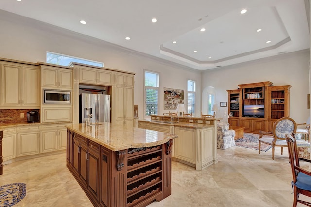 kitchen featuring appliances with stainless steel finishes, a center island with sink, a tray ceiling, and cream cabinets