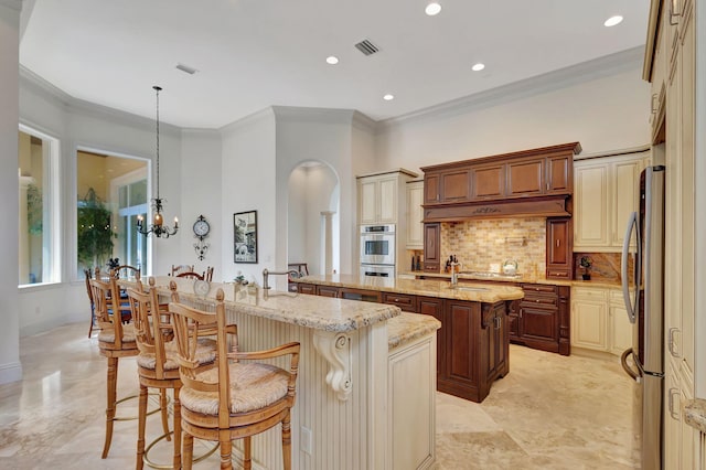 kitchen featuring light stone countertops, appliances with stainless steel finishes, a breakfast bar, a kitchen island with sink, and hanging light fixtures