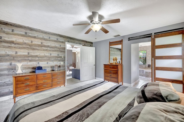 bedroom with ceiling fan, a barn door, wooden walls, and connected bathroom