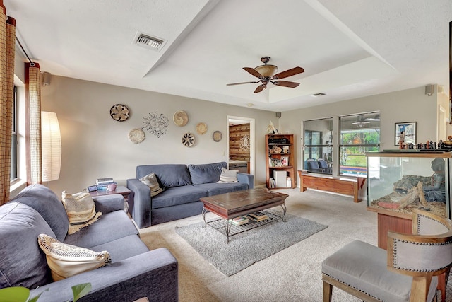 carpeted living room with a tray ceiling and ceiling fan