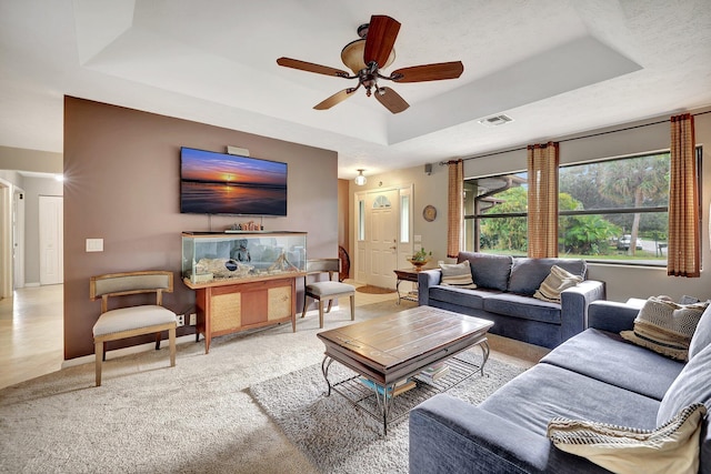 living room with light carpet, a textured ceiling, a tray ceiling, and ceiling fan