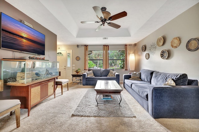 carpeted living area featuring a tray ceiling and a ceiling fan