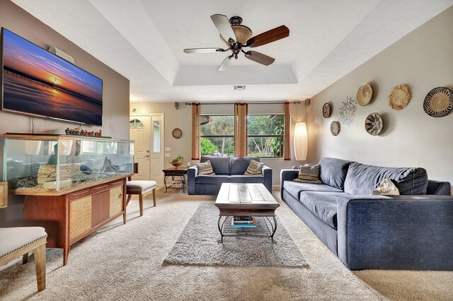 carpeted living area with visible vents, a ceiling fan, a textured ceiling, baseboards, and a raised ceiling