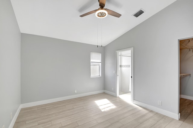 unfurnished bedroom featuring ceiling fan, vaulted ceiling, a walk in closet, a closet, and light wood-type flooring