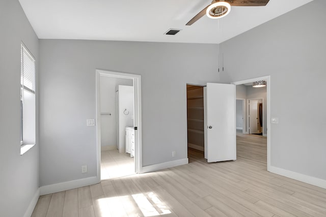 unfurnished bedroom with ensuite bath, ceiling fan, light hardwood / wood-style floors, a spacious closet, and vaulted ceiling