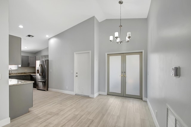 foyer entrance featuring french doors, sink, high vaulted ceiling, light wood-type flooring, and a notable chandelier