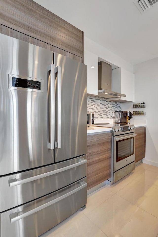 kitchen featuring white cabinets, wall chimney range hood, decorative backsplash, light tile patterned floors, and stainless steel appliances