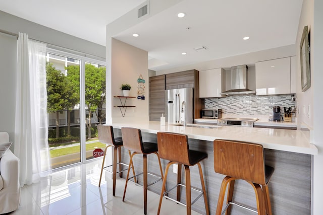 kitchen featuring wall chimney exhaust hood, a kitchen bar, light tile patterned floors, and stainless steel appliances