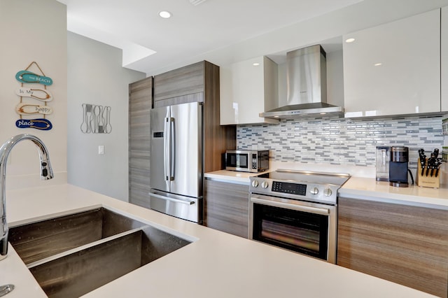 kitchen featuring sink, wall chimney exhaust hood, decorative backsplash, white cabinets, and appliances with stainless steel finishes