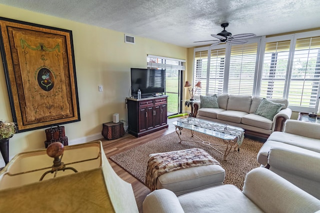 living room featuring visible vents, a ceiling fan, a textured ceiling, wood finished floors, and baseboards