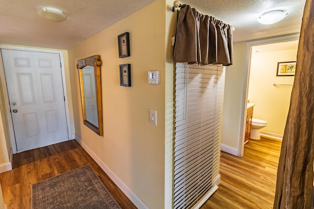 corridor featuring a textured ceiling, wood finished floors, and baseboards