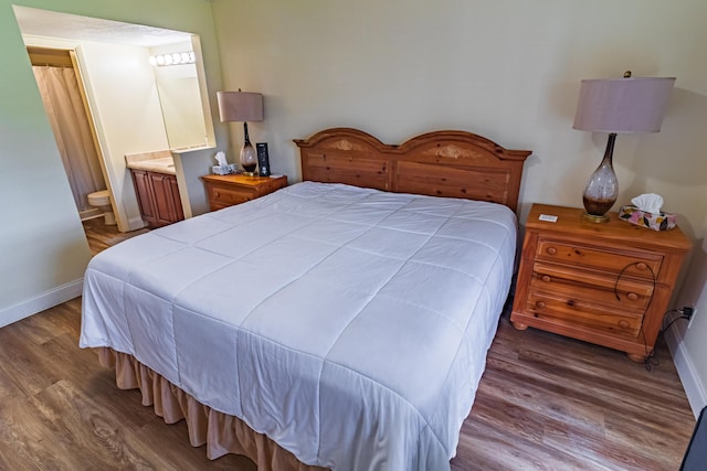 bedroom with ensuite bath, baseboards, and wood finished floors