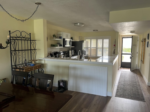 kitchen featuring stainless steel appliances, tasteful backsplash, kitchen peninsula, white cabinets, and hardwood / wood-style flooring