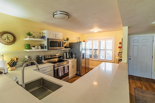 kitchen with appliances with stainless steel finishes, a sink, light stone counters, and open shelves