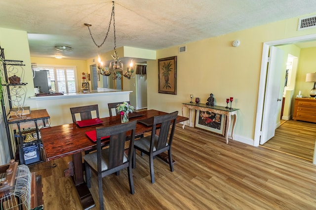 dining space featuring baseboards, a textured ceiling, visible vents, and wood finished floors